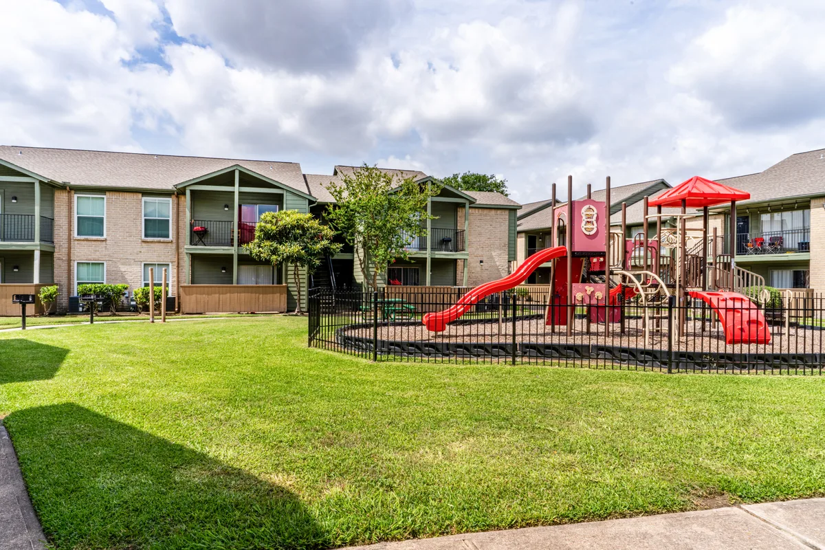 Fenced children's playground with a red slide beside the residential buildings