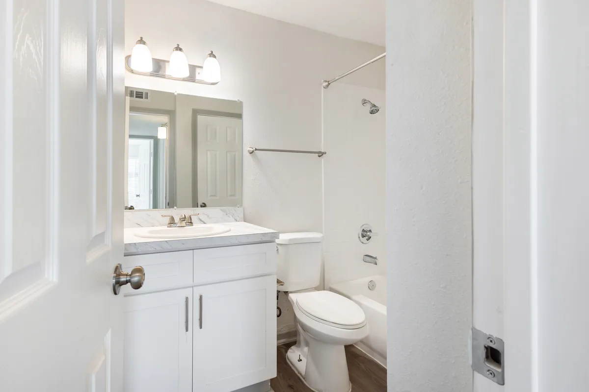 White bathroom with a shaker vanity, marble-look counter, and a tiled tub-shower