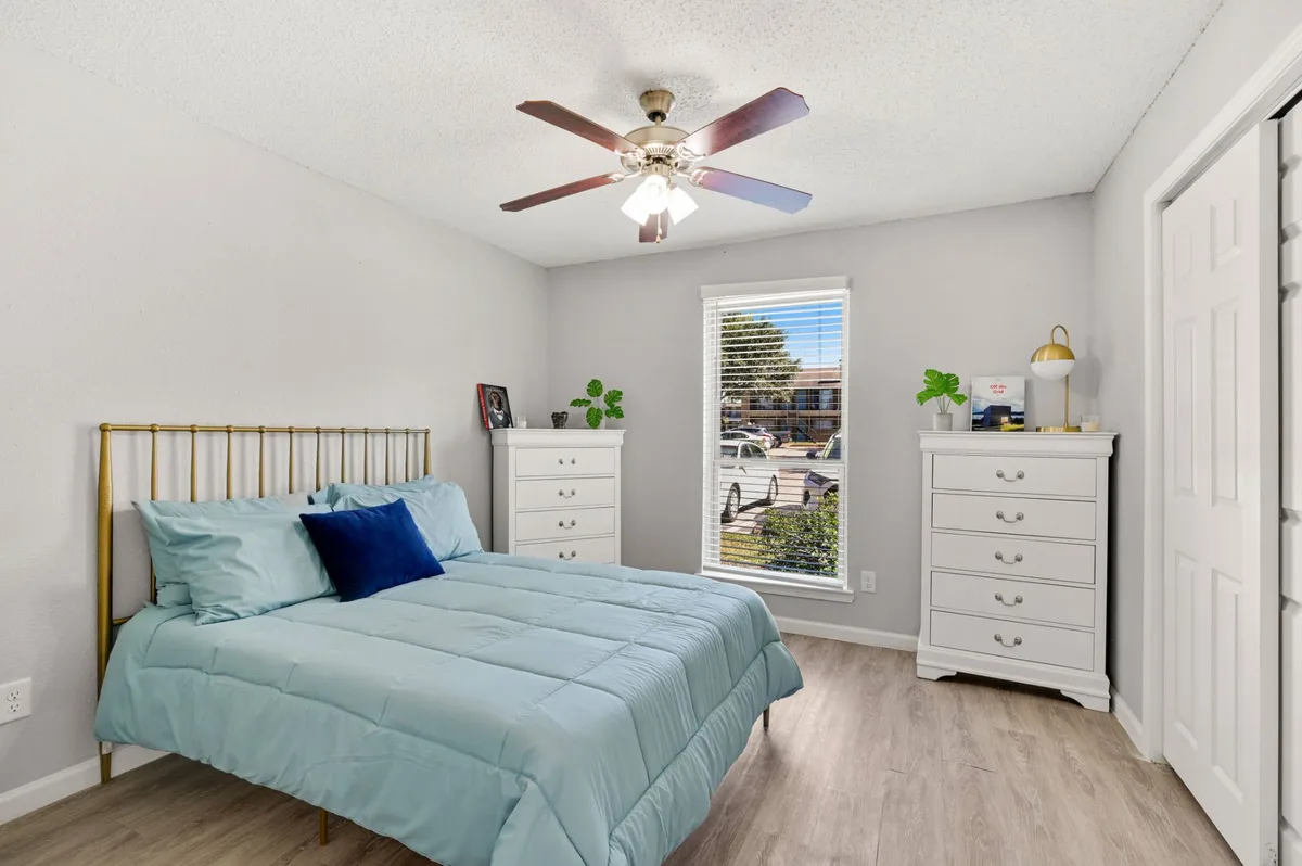 Bedroom with a lit ceiling fan, wood-look flooring, and two white dressers by a window
