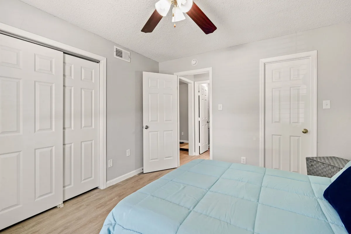 Bedroom with a ceiling fan, sliding closet doors, and a hallway view through an open door