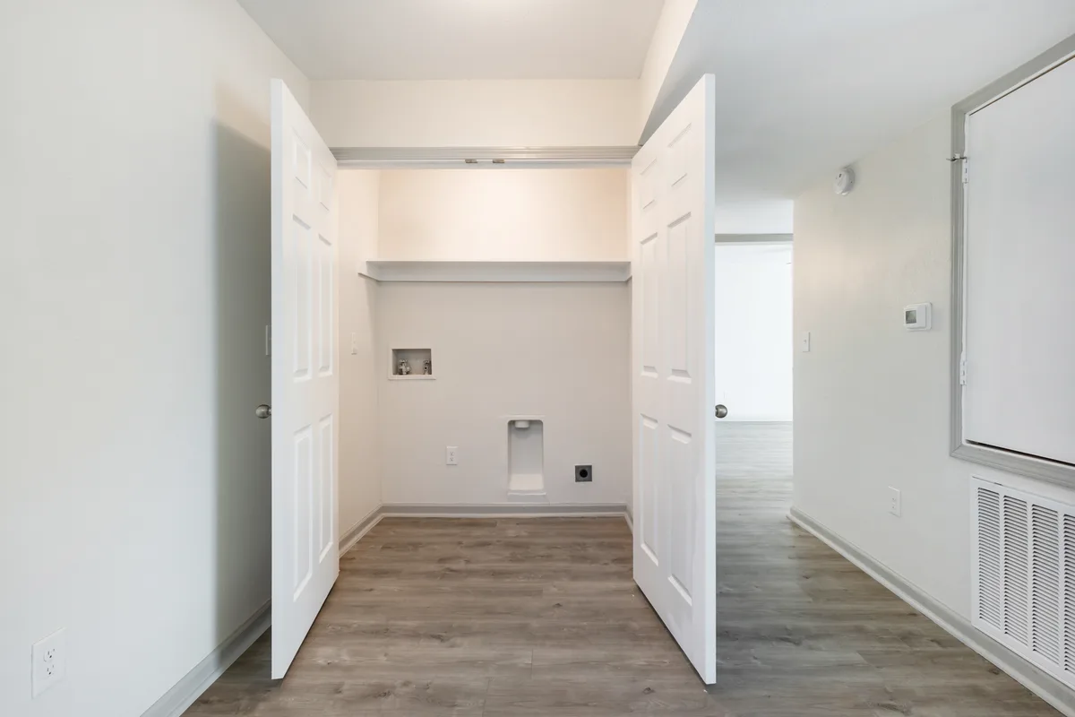 Open double-door closet with a shelf, hanging rod, and washer/dryer connections