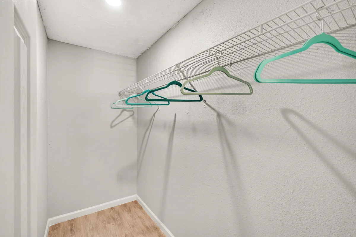 Walk-in closet with a white wire shelf and hanging rod over wood-look flooring