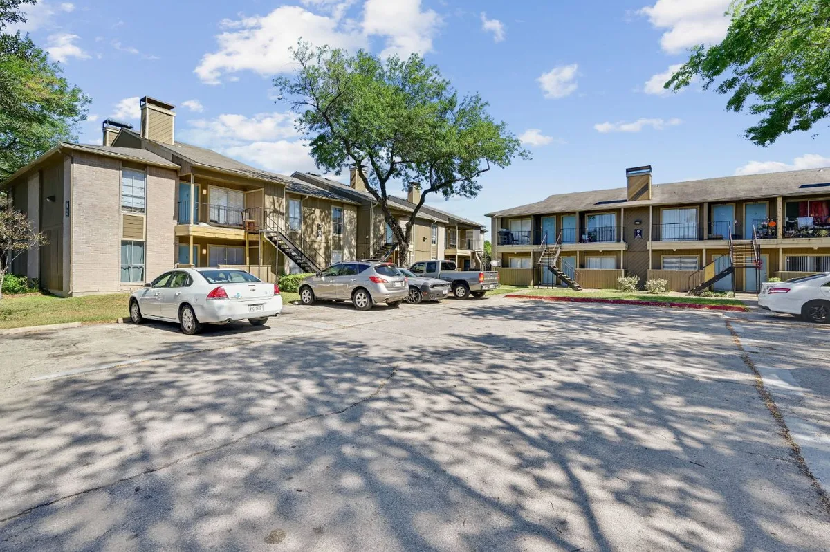 Tree-shaded courtyard and parking between two-story tan-brick apartment buildings