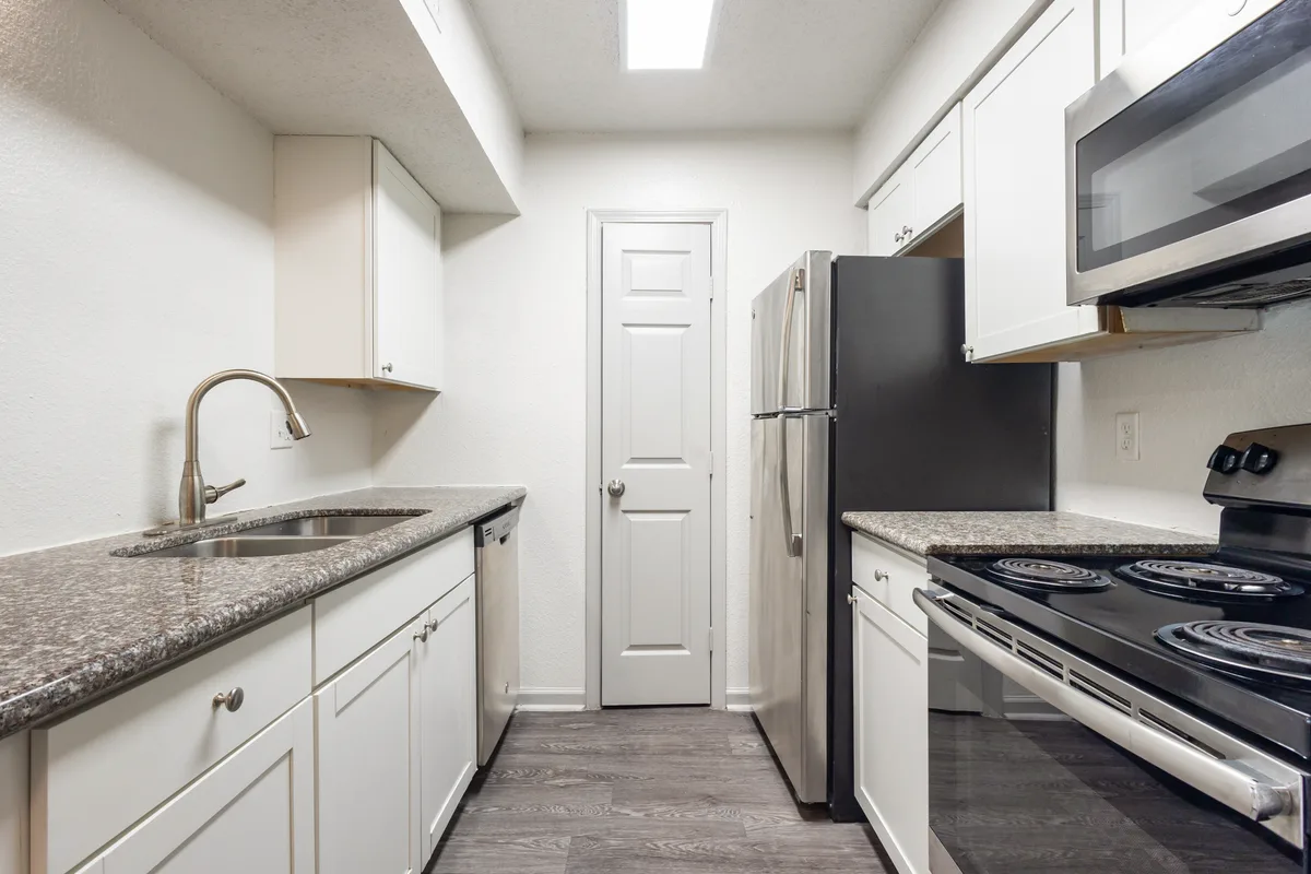 Galley kitchen with white cabinets, granite-look countertops, and stainless-steel appliances