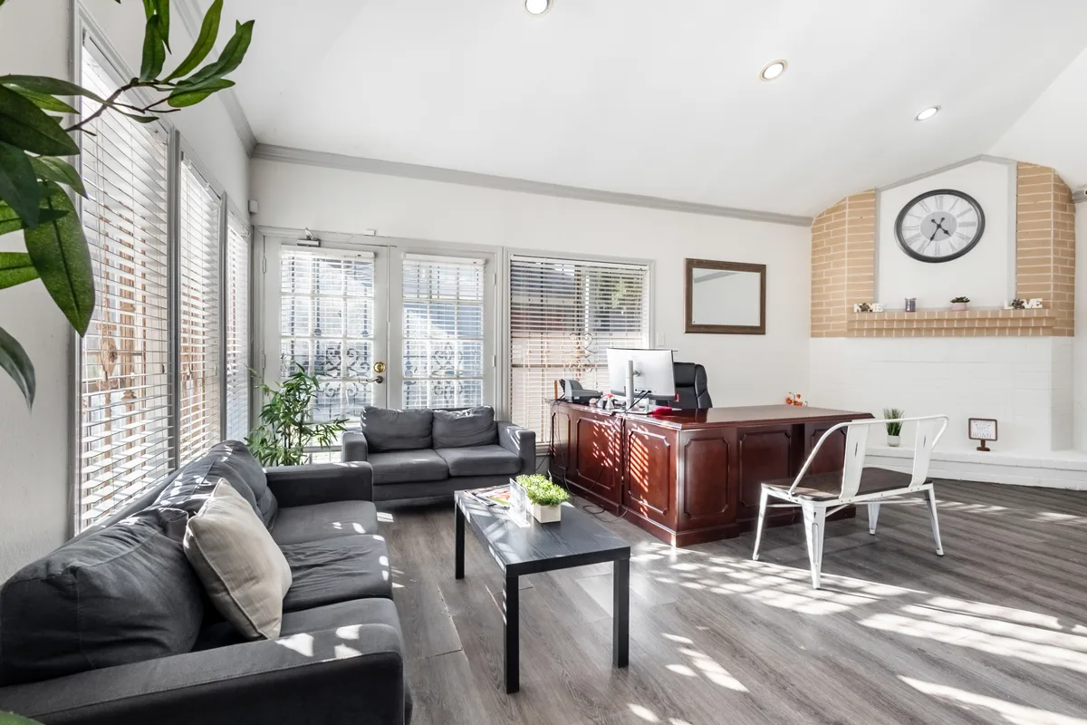 Sunlit leasing office with gray sofas, a wood reception desk, and a wall clock
