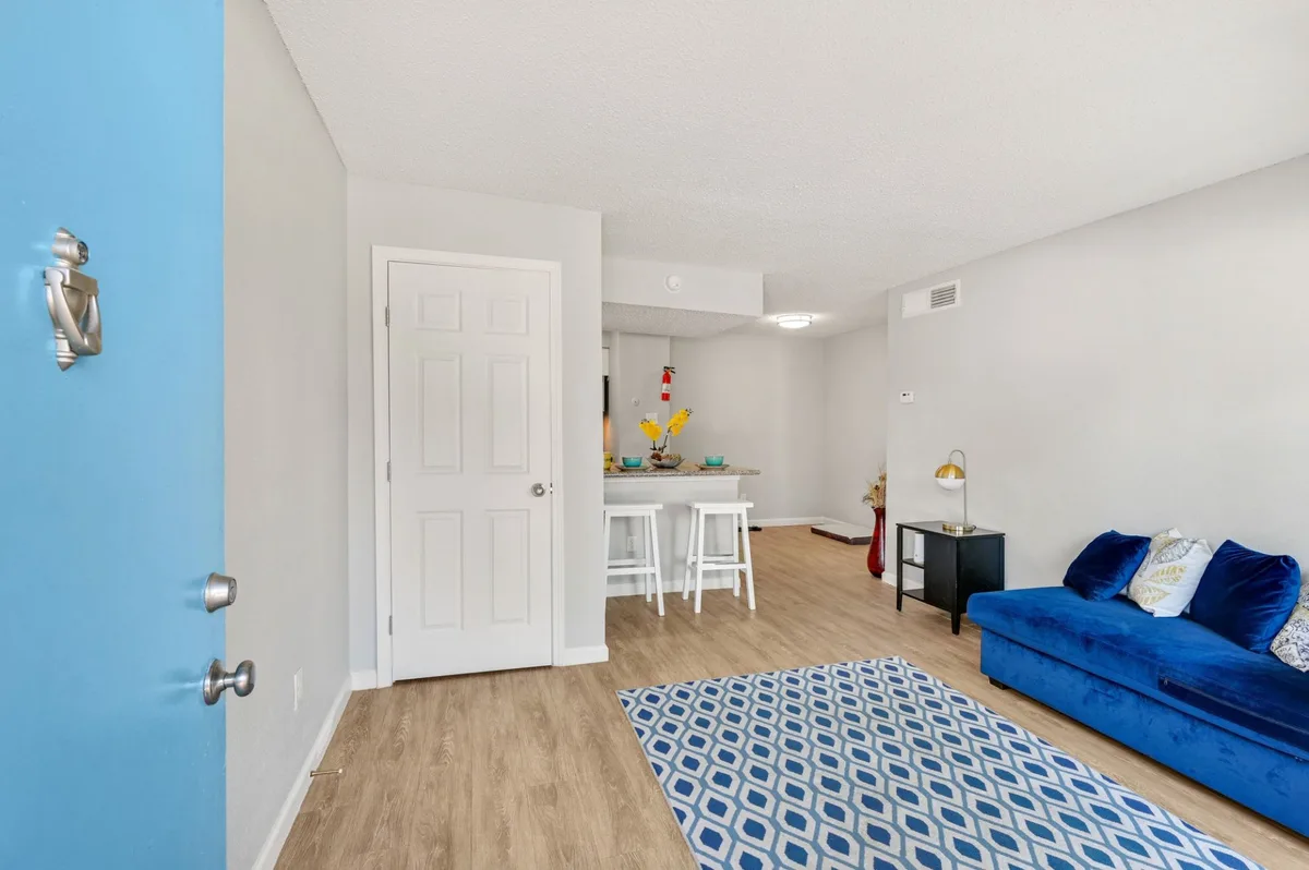 Living room with a blue front door, wood-look flooring, and a granite breakfast bar with stools