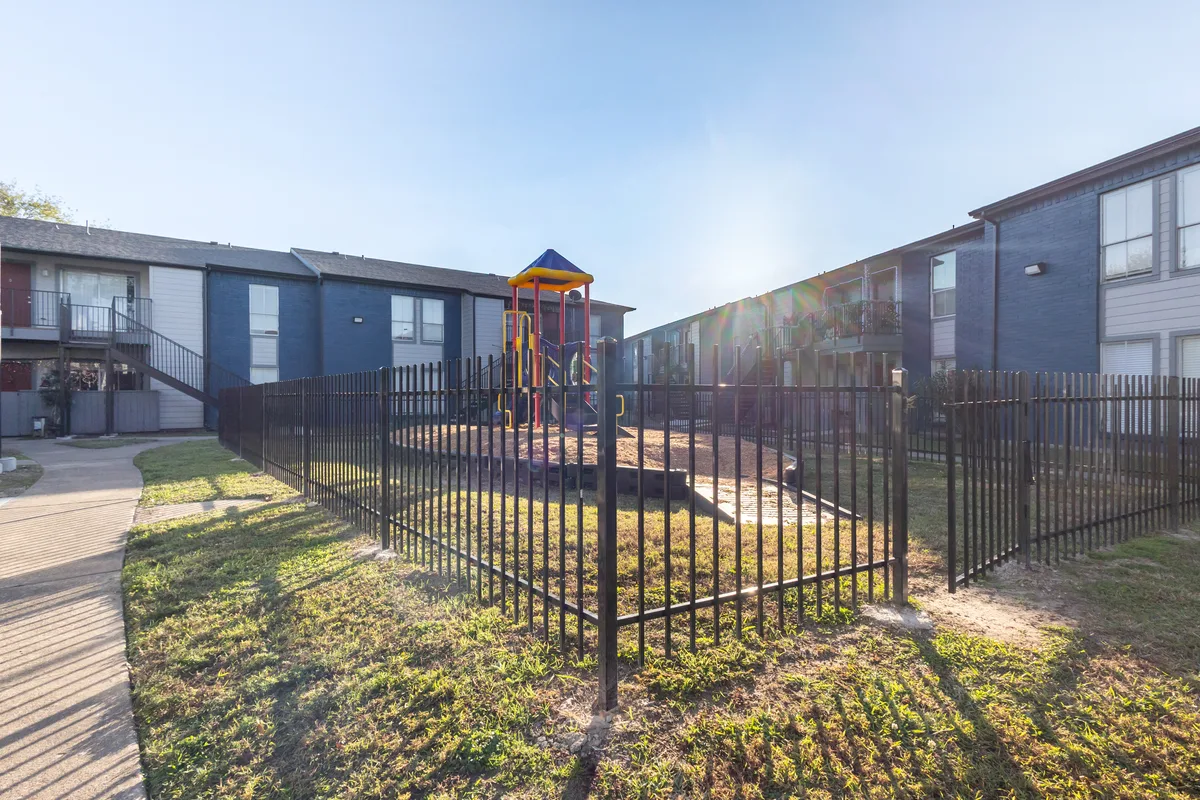 Fenced playground with a colorful play structure, surrounded by apartment buildings