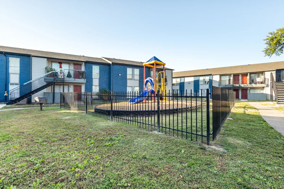 Playground surrounded by a fence in the apartment community, with blue buildings behind it