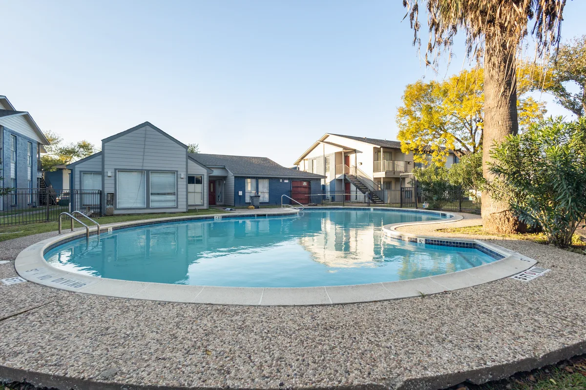 Swimming pool at dusk surrounded by apartment buildings, a palm tree, and a pebbled concrete deck