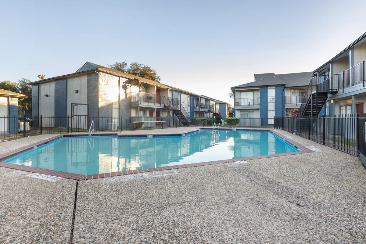 Swimming pool surrounded by apartment buildings, with clear blue water and a textured pavement deck