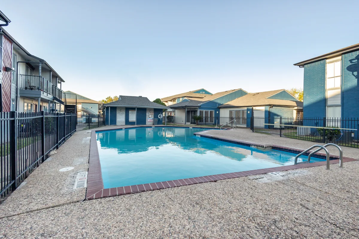 Swimming pool surrounded by textured concrete and fencing, with apartment buildings in the background