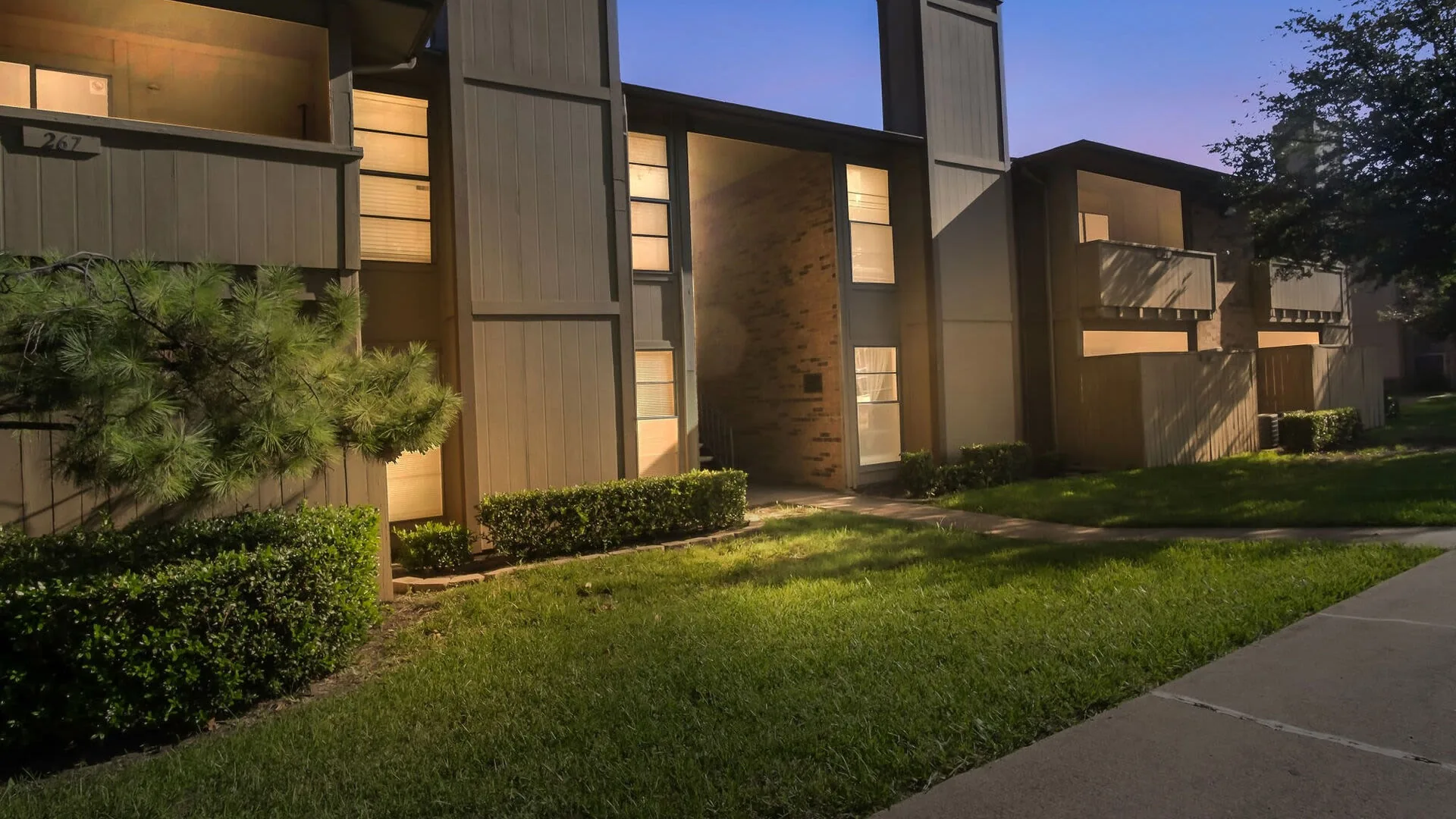 Two-story buildings with brick accents and lit balconies at dusk along a landscaped walkway