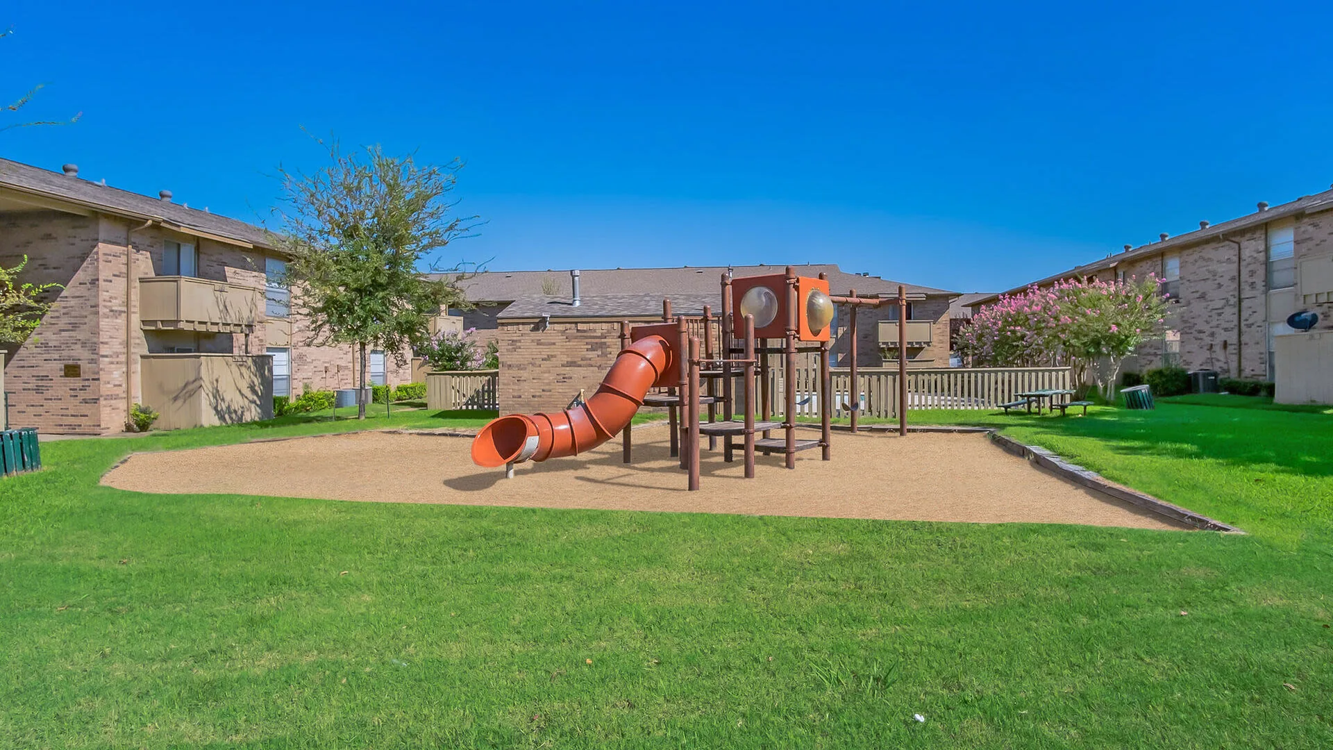 Playground with slides and climbing structure on a sand pad beside the buildings