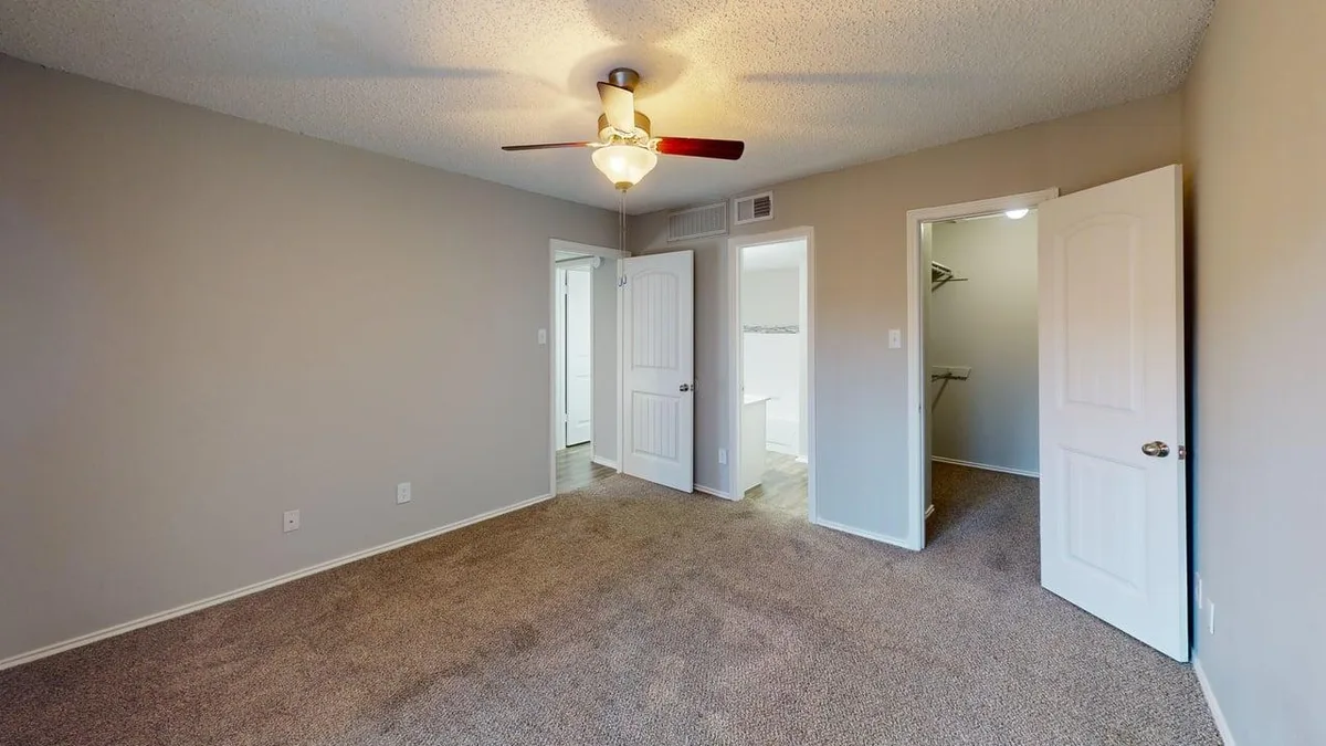 Carpeted bedroom with a lighted ceiling fan and walk-in closet access