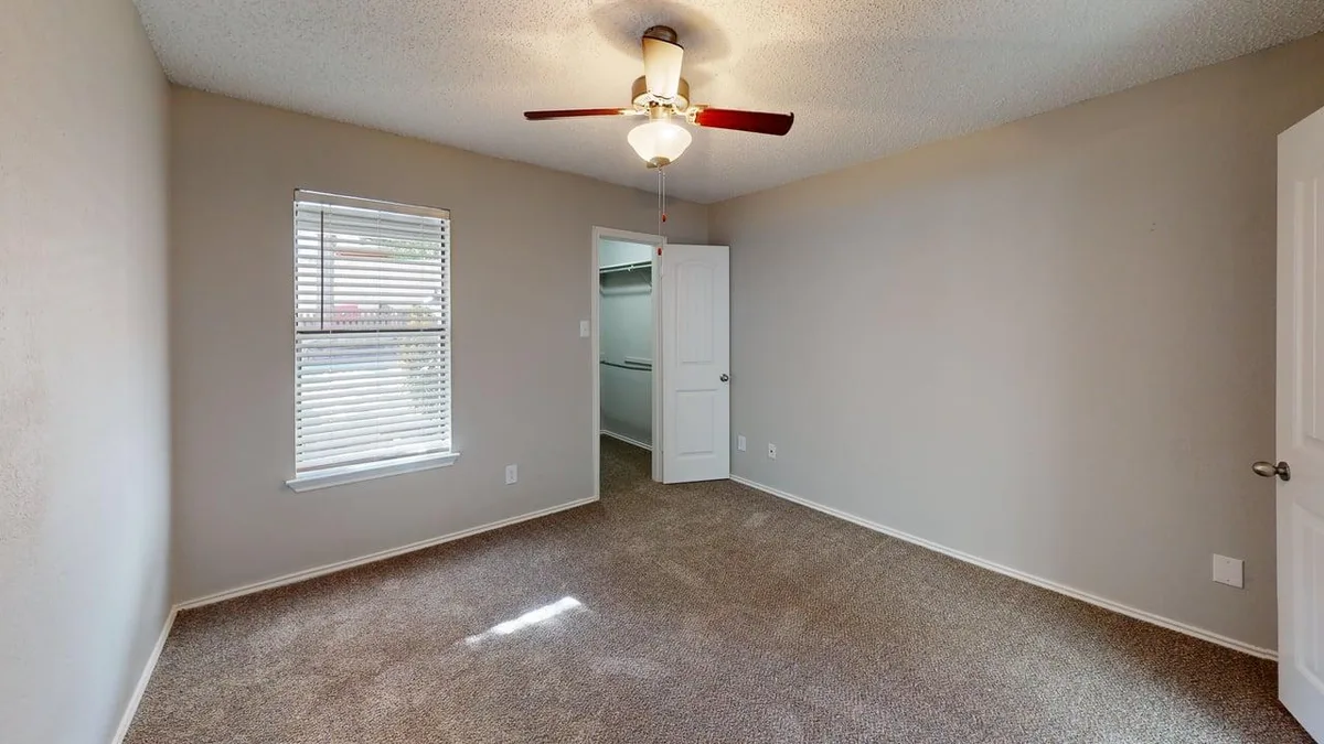 Carpeted bedroom with a bright window, ceiling fan, and walk-in closet