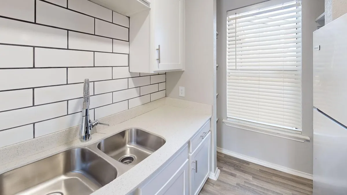 Galley kitchen with white subway tile, quartz-style counters, and a stainless refrigerator