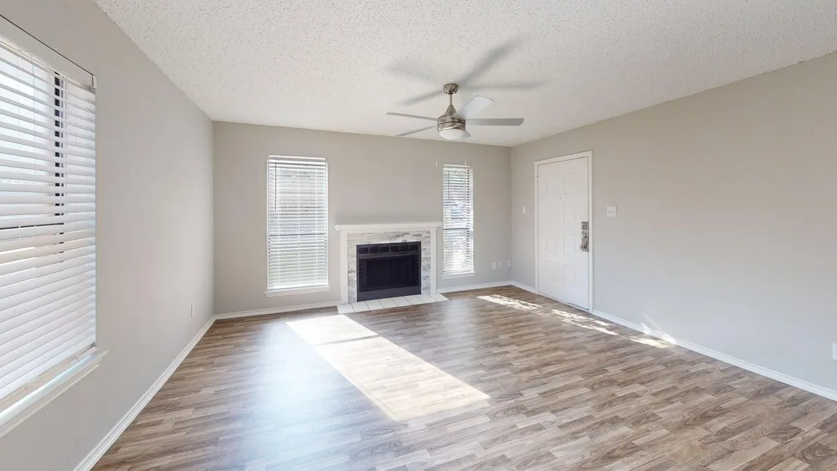 Sunlit living room with a corner fireplace, front entry, and wood-look floors