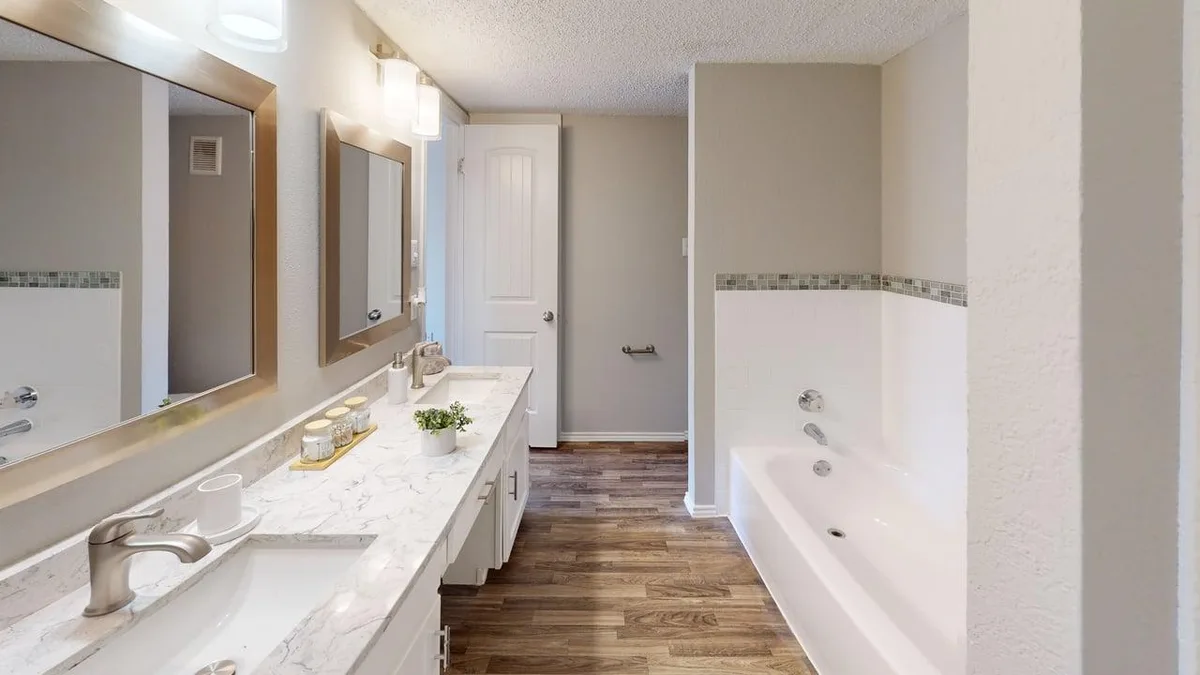 Dual-vanity bathroom with marble-look counters, a soaking tub, and wood-look flooring