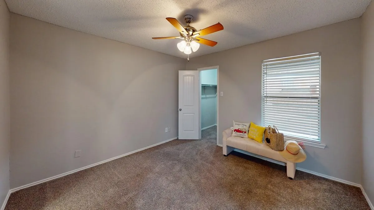Carpeted bedroom with a ceiling fan, walk-in closet, and staged bench seating