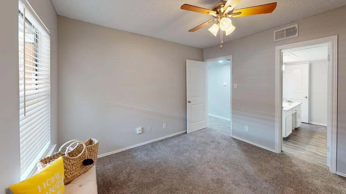 Carpeted bedroom with a bright window and doorways to the hall and bath