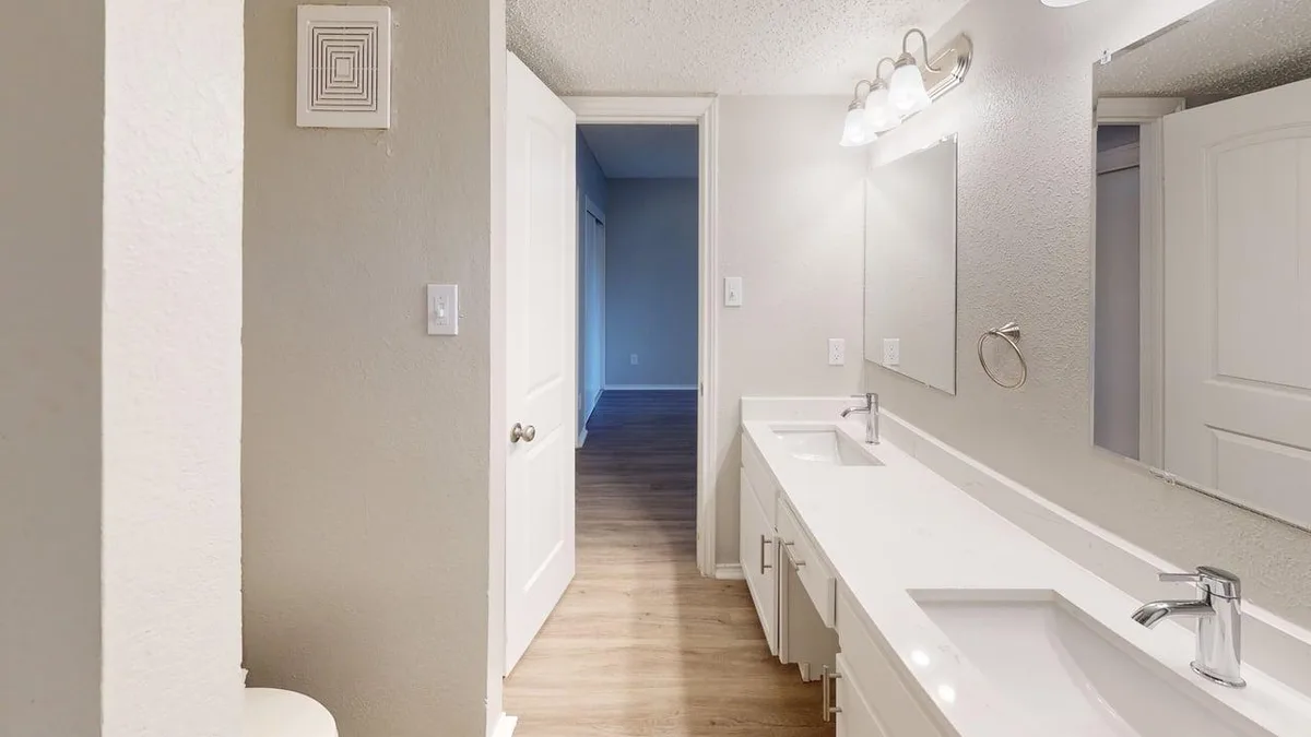 Dual-vanity bathroom with quartz counters, a framed mirror, and wood-look flooring