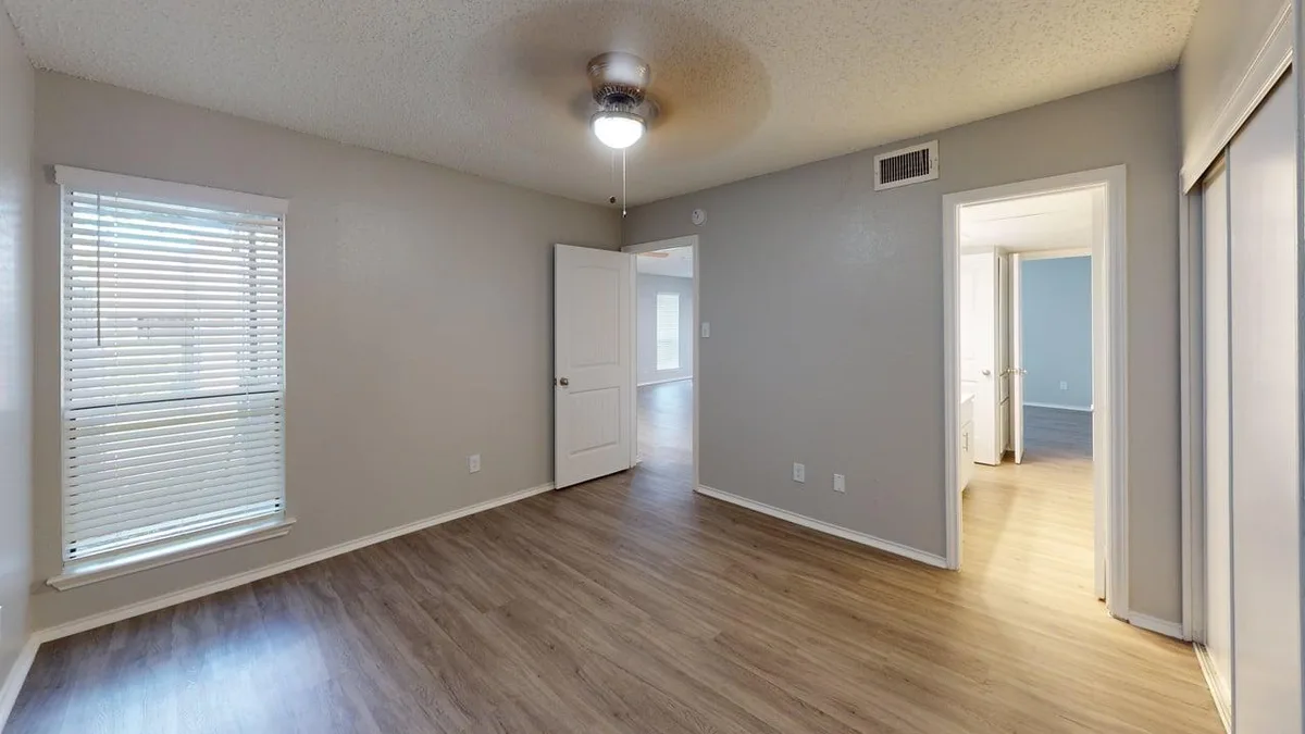 Wood-floored bedroom with a bright window and doorways to the bath and closet
