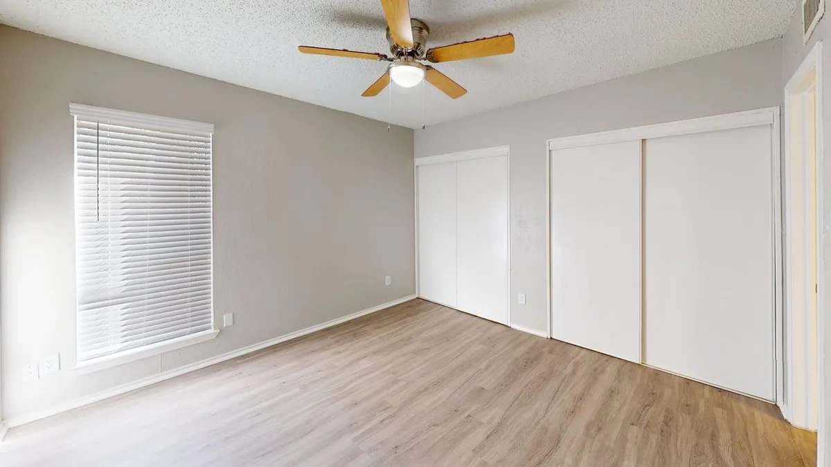 Wood-floored bedroom with two closets, a ceiling fan, and a window