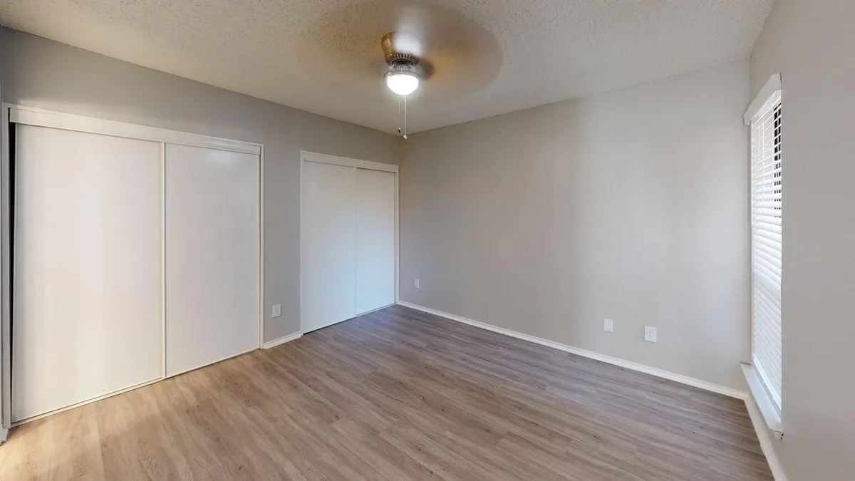 Carpeted bedroom with a large window, ceiling fan, and dual sliding closets