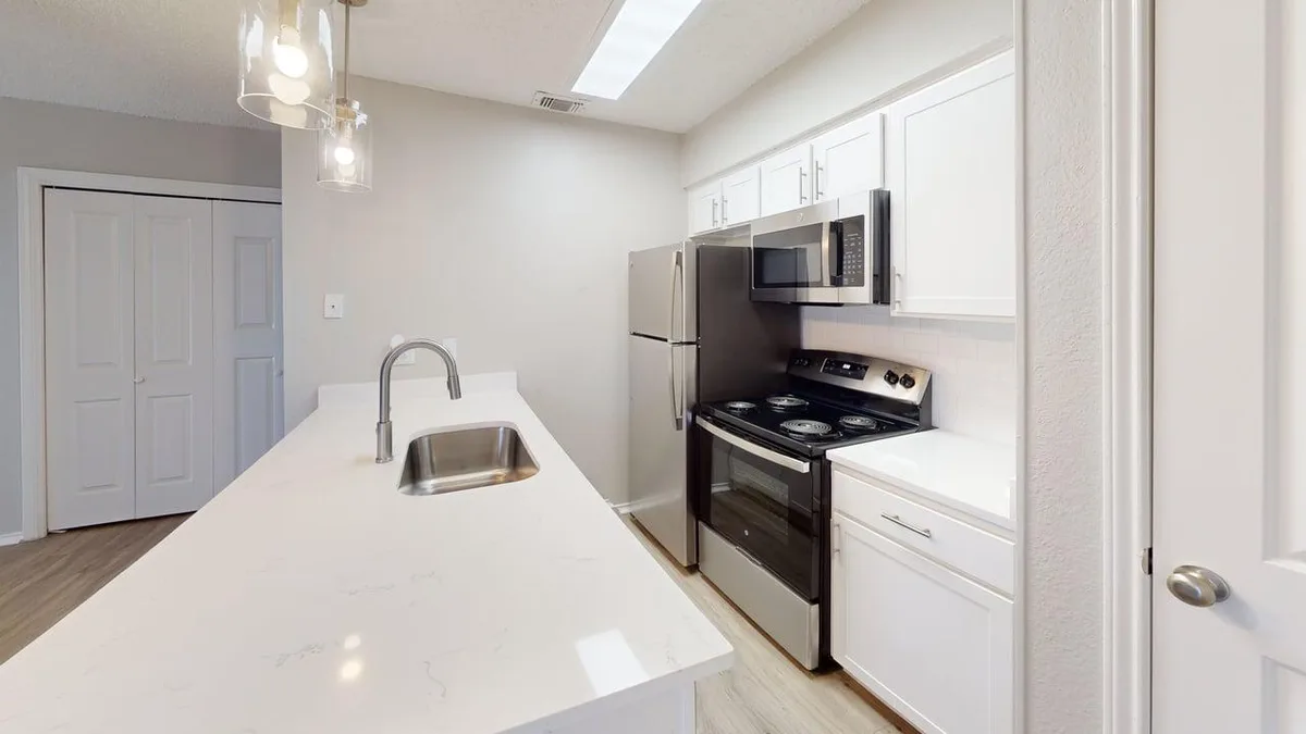 Galley kitchen with quartz counters, stainless appliances, and a pantry closet