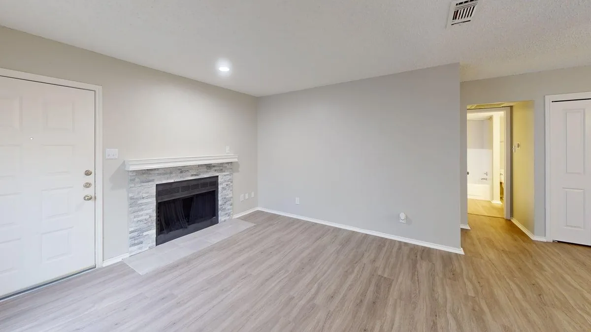 Living room with a stacked-stone fireplace, wood-look floors, and a hallway to the bath