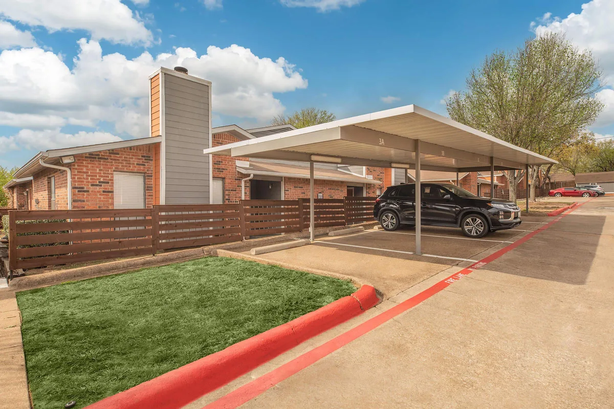 Covered resident carport beside a brick building with a landscaped lawn