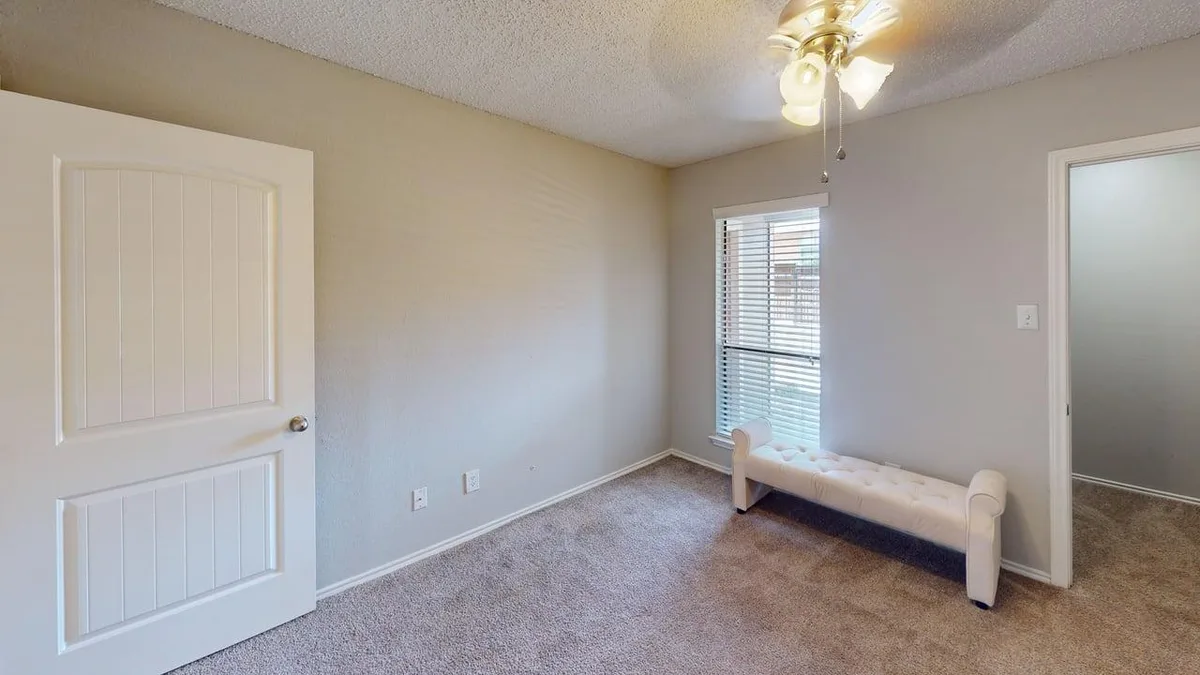 Carpeted bedroom with a bright window, ceiling fan, and staged bench