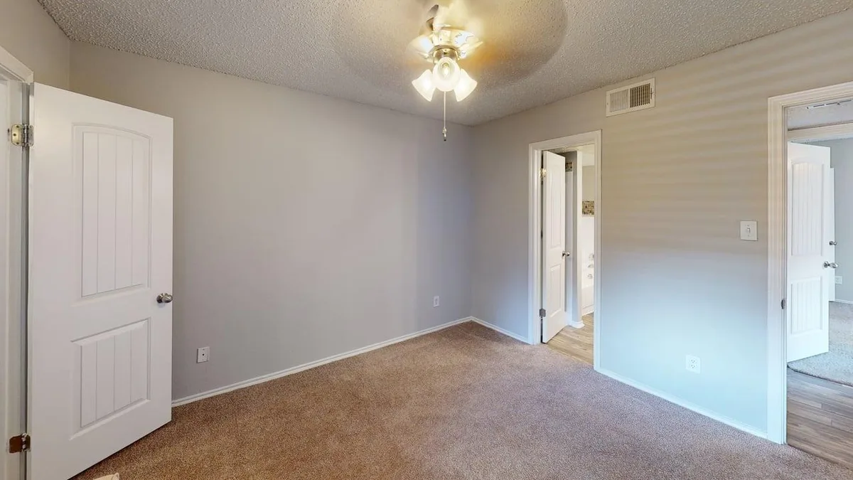 Carpeted bedroom with a ceiling fan and doorway to the private bath