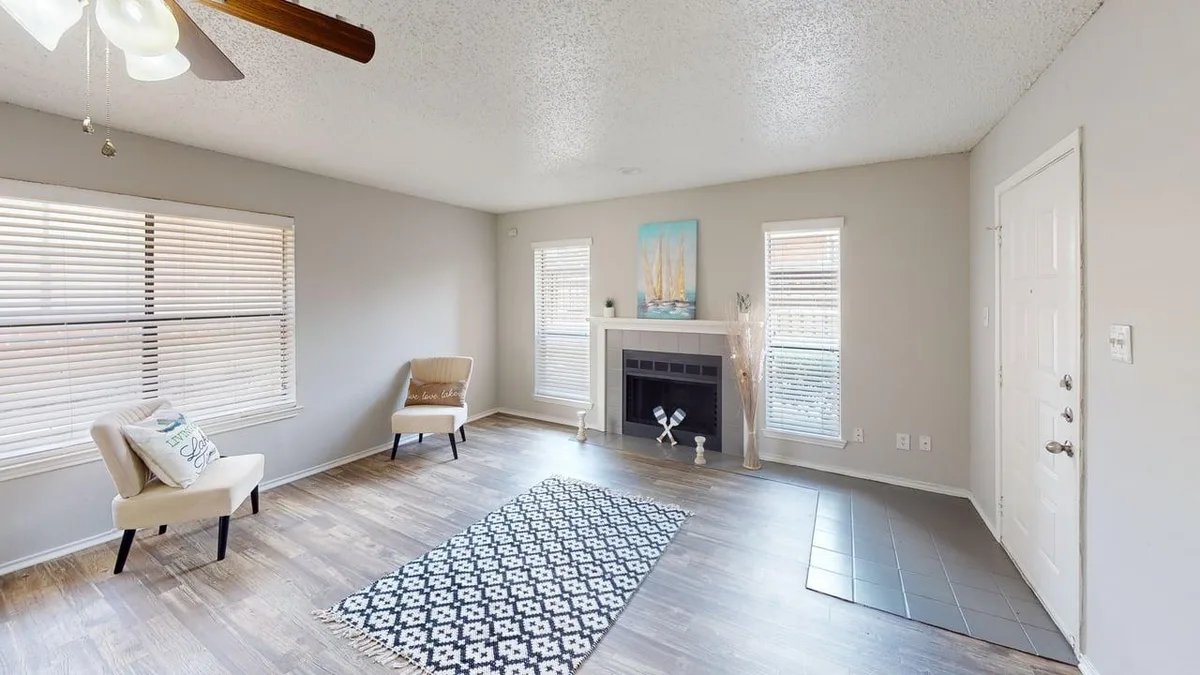 Living room with a tiled corner fireplace, dual windows, and staged seating