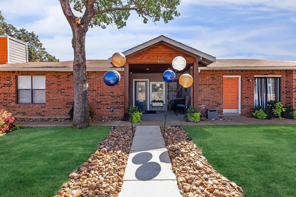 Brick leasing office and clubhouse entrance with a stone-lined walkway and green lawn