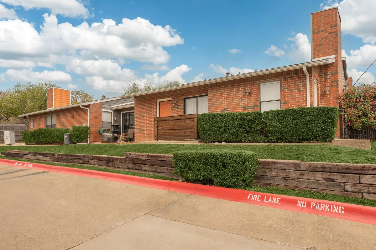 Single-story brick apartment building at Villas at Lake Arlington with a manicured lawn and clipped hedges