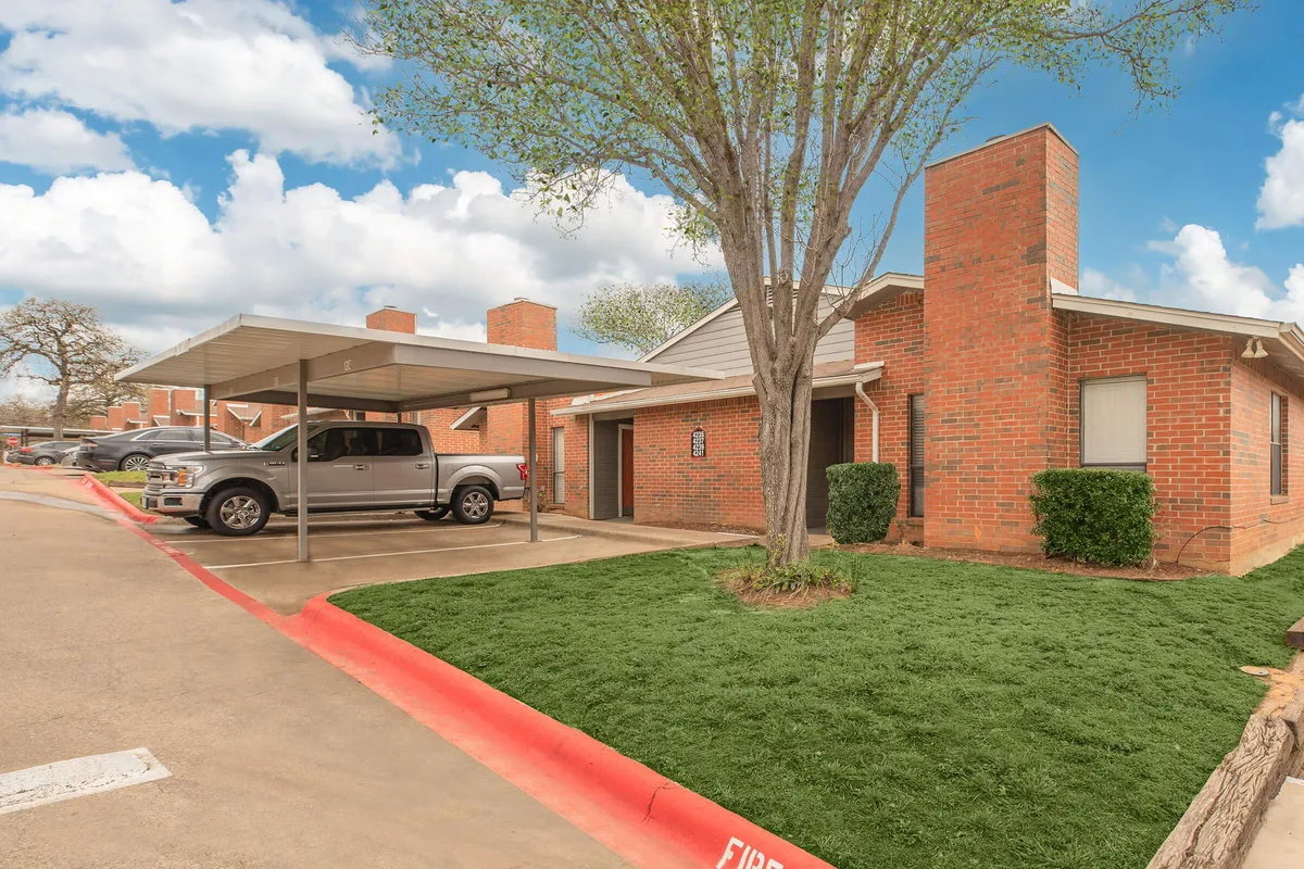 Brick apartment building with a covered resident carport and mature shade trees