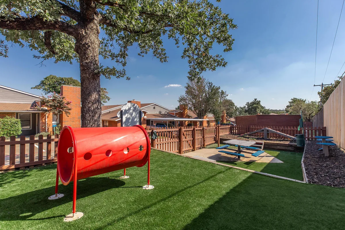 Children's play structure and picnic tables in a fenced artificial-turf courtyard