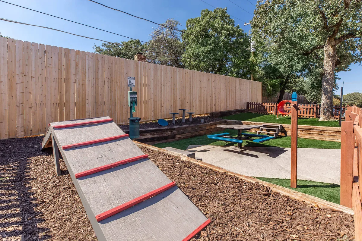 Playground with a ramped play structure, picnic tables, and shaded seating on turf