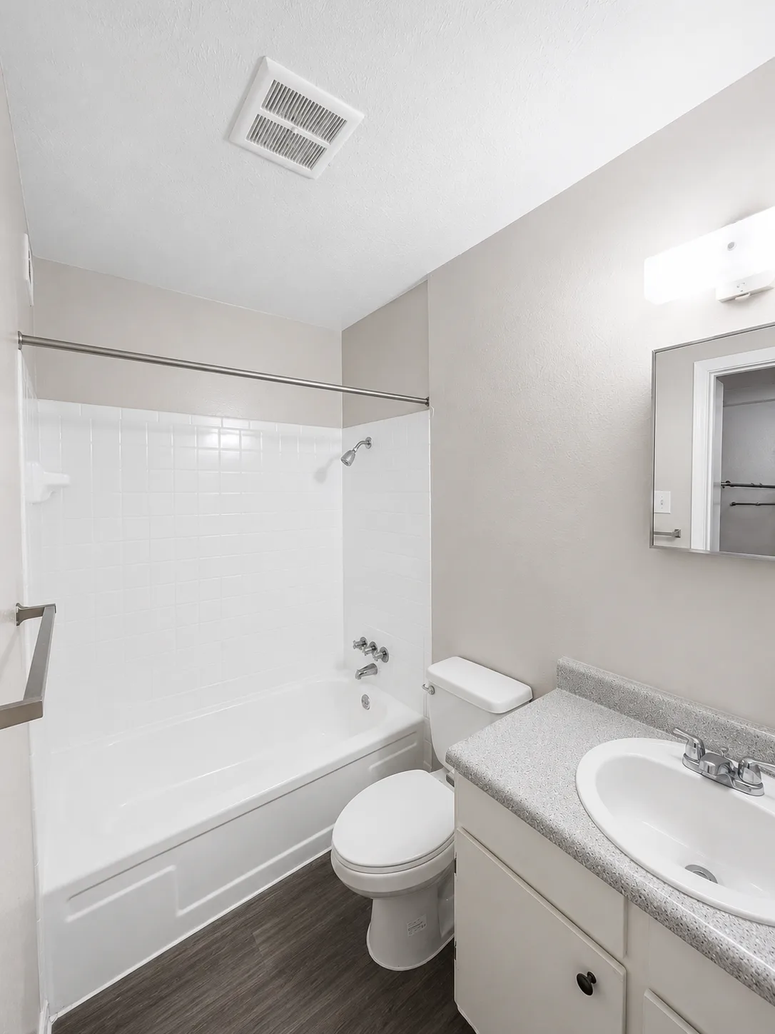 A1 bathroom with a white-tiled tub and shower, a speckled-top vanity with a framed mirror, and wood-look flooring