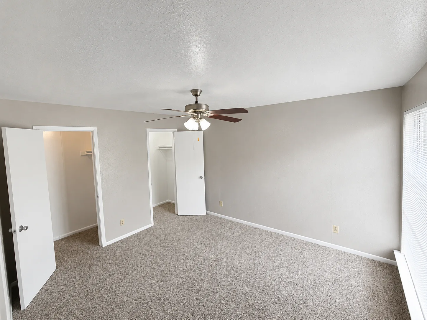 Empty carpeted B1 bedroom with a ceiling fan and two closets, one a walk-in with a shelf and one with a hanging rod