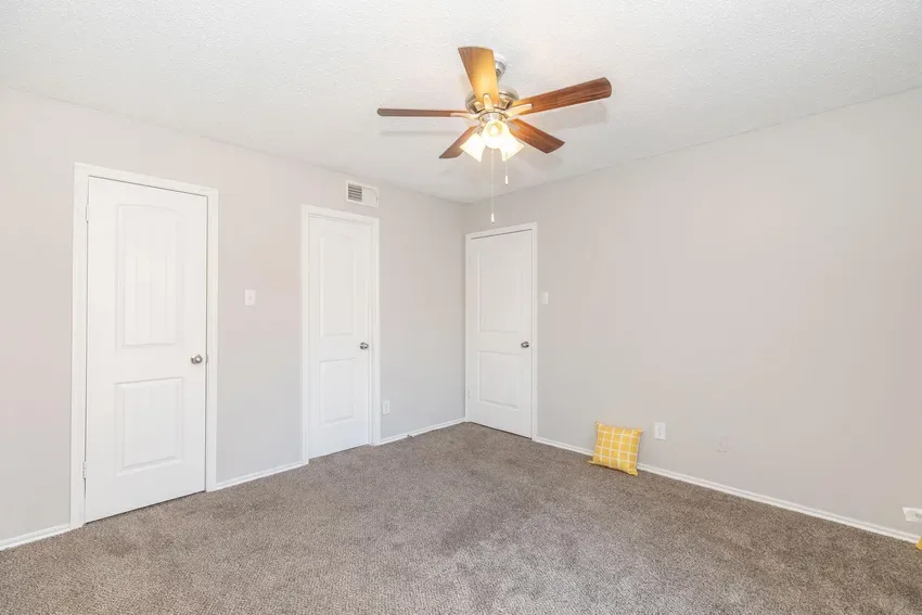 Carpeted bedroom with multiple closet doors and a ceiling fan