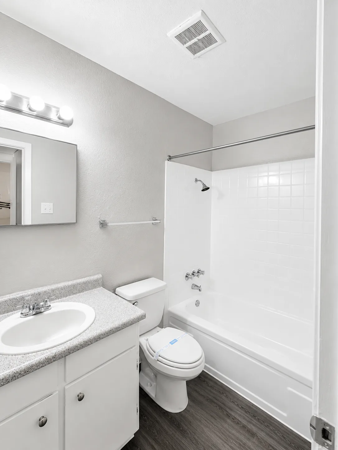 C1 bathroom with a white-tiled tub and shower, a speckled-top vanity with a framed mirror, and wood-look flooring