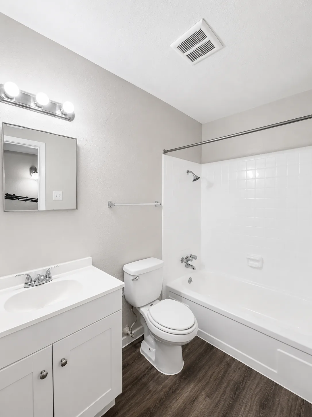 Second C1 bathroom with a white-tiled tub and shower, a white-top vanity with a framed mirror, and wood-look flooring
