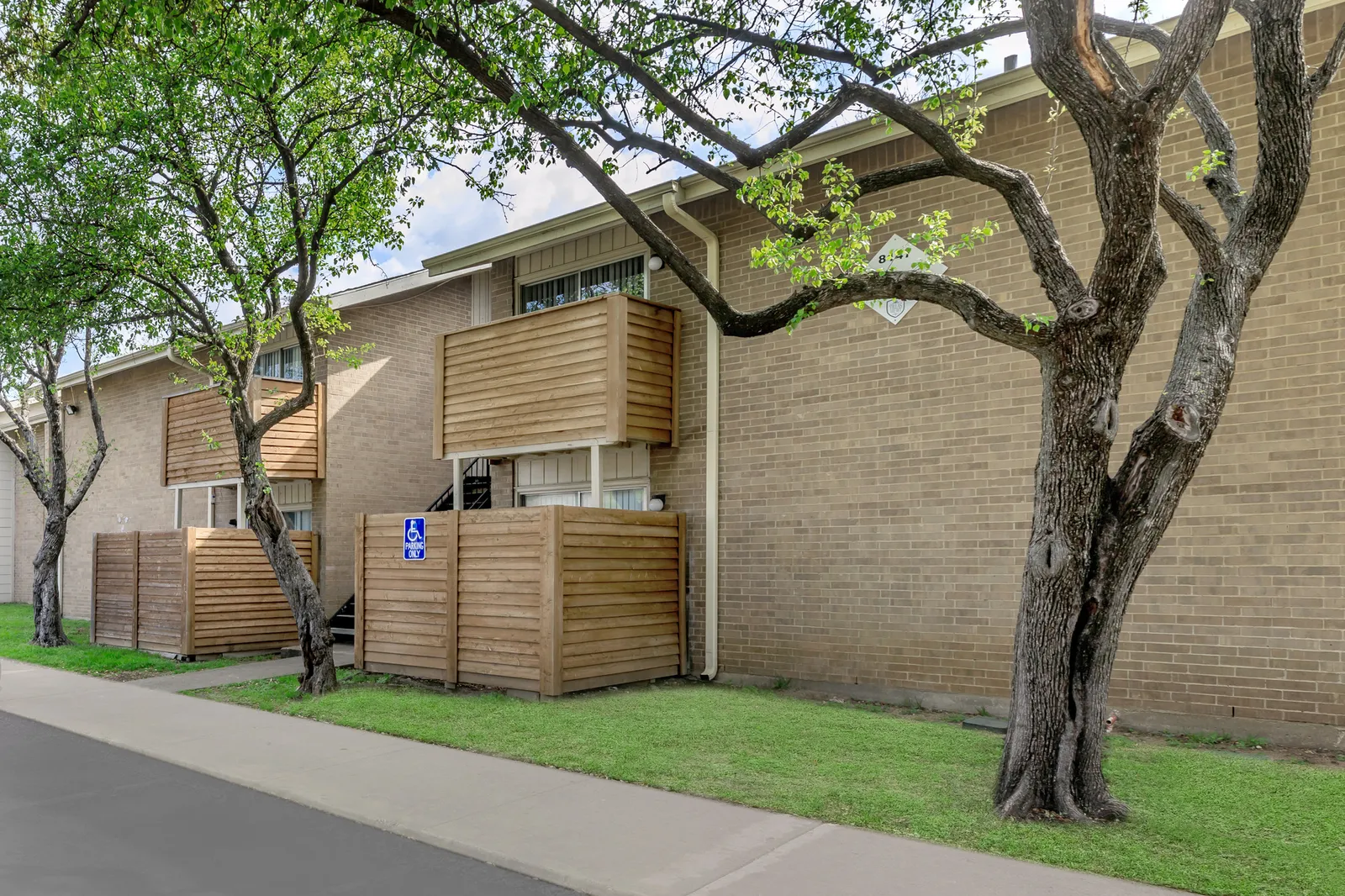 Tan brick building with wood-screened patios and balconies beneath a mature shade tree