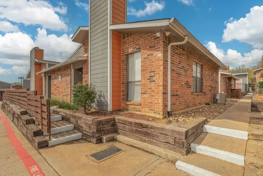 Red-brick townhome-style entries with timber-edged planting beds along the walkway