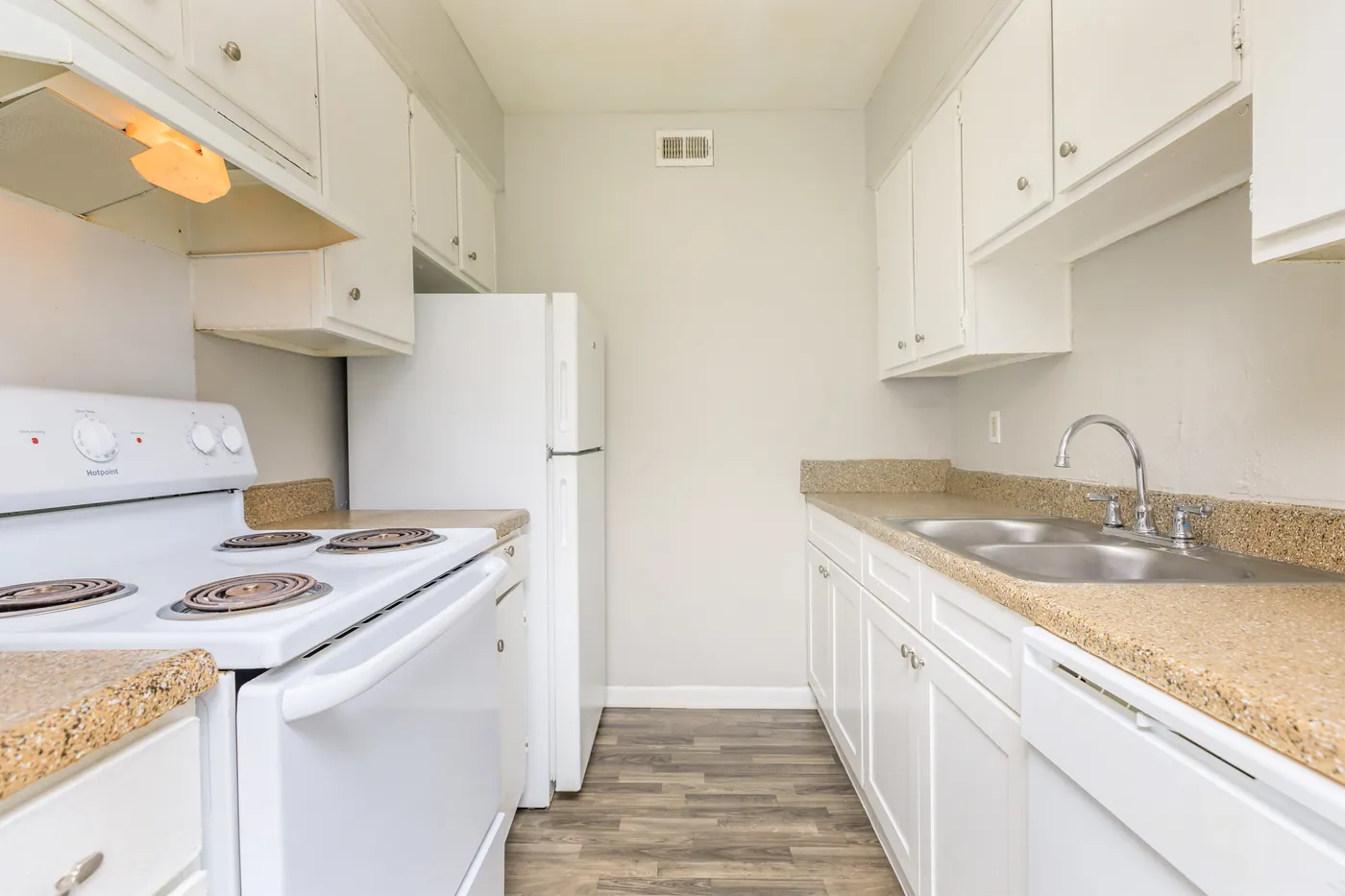 Galley kitchen with white cabinets, electric range, and double sink