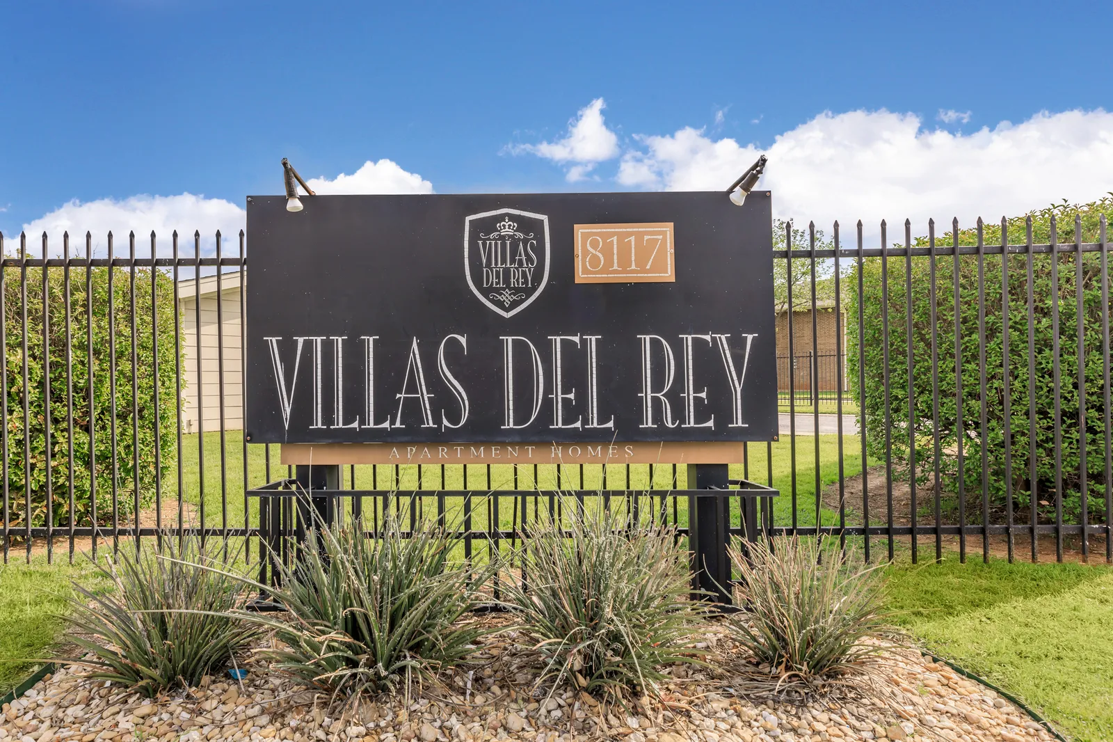 Villas Del Rey monument sign in front of the black perimeter fence and landscaped lawn