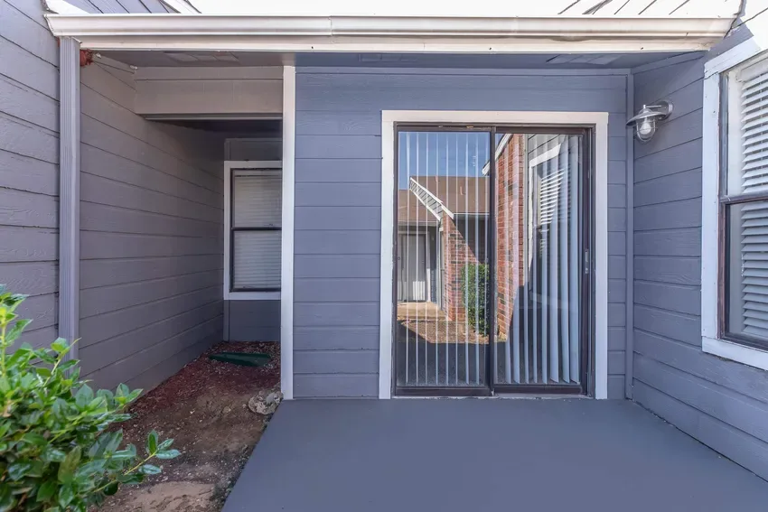 Private enclosed patio with gray siding and a sliding-glass door entry