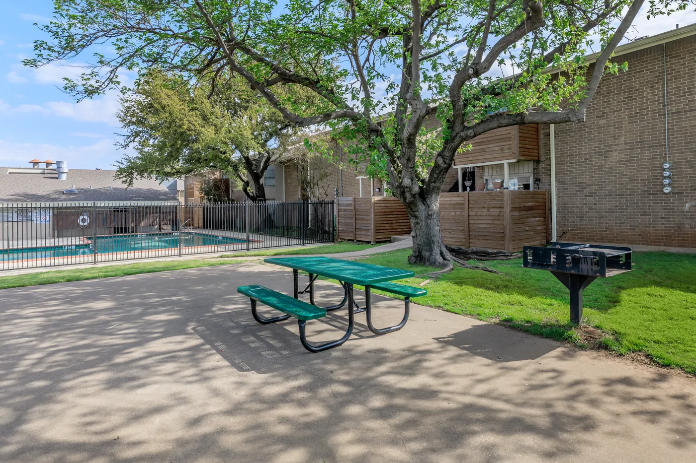 Picnic table and barbecue grill shaded by a mature tree beside the pool